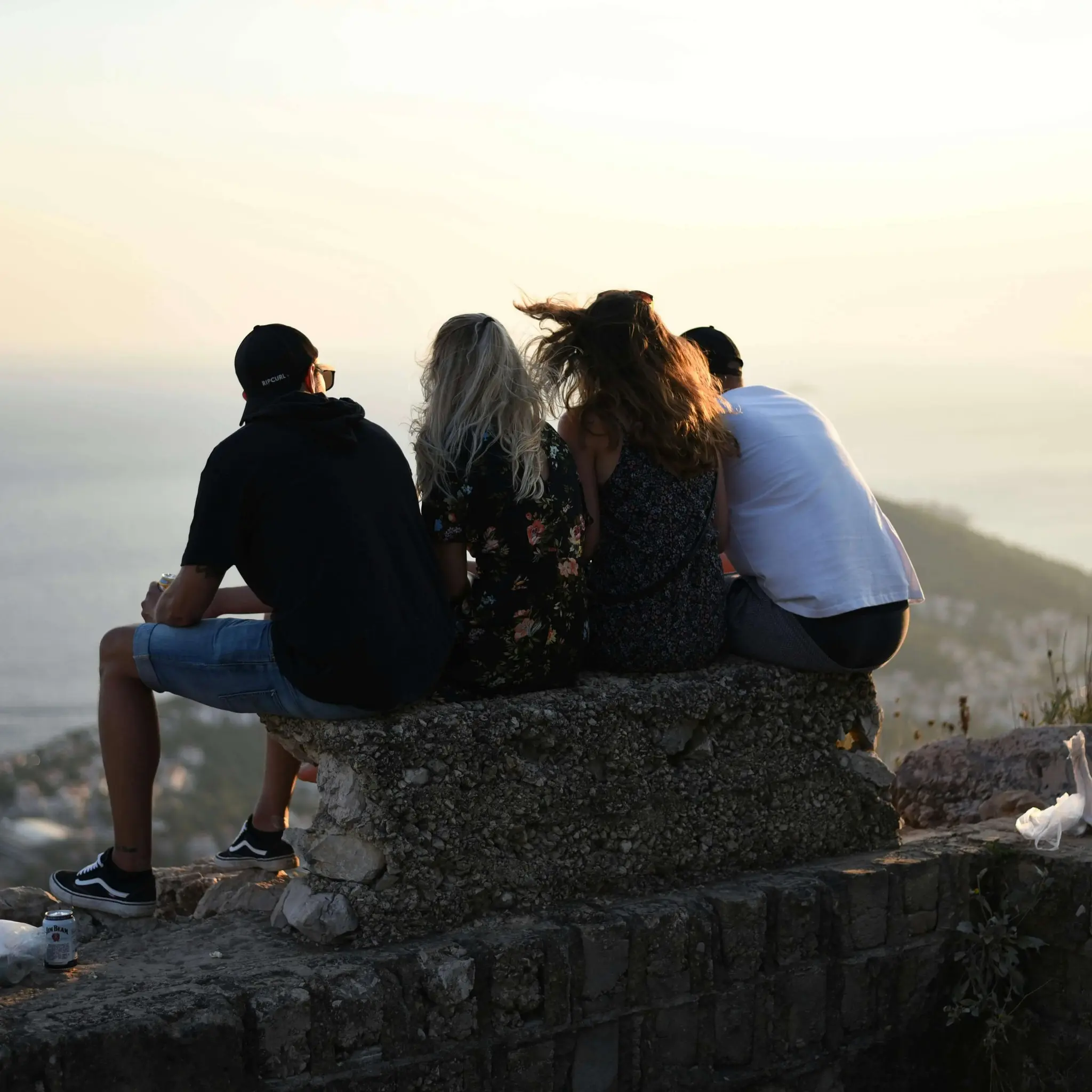 A group of friends sitting on a wall looking at the ocean, representing connection and community.