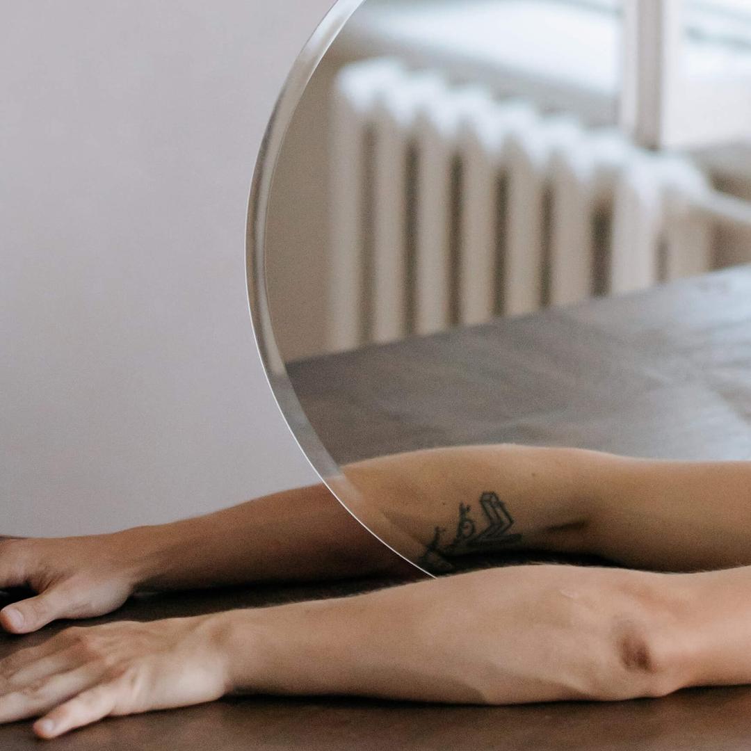 A circular mirror with the reflection of an arm in front.