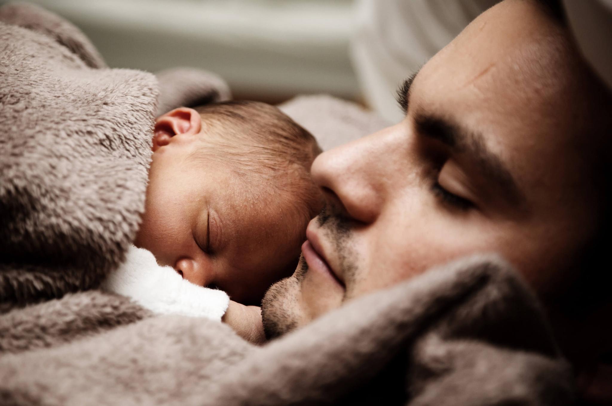 A man who recently became a parent, snuggling a newborn child.